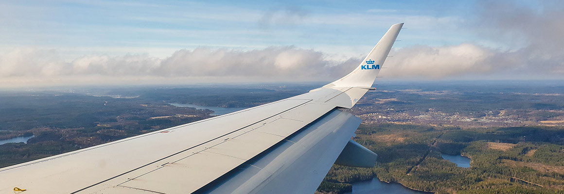 Vleugel van een KLM vliegtuig boven een bosrijk gebied