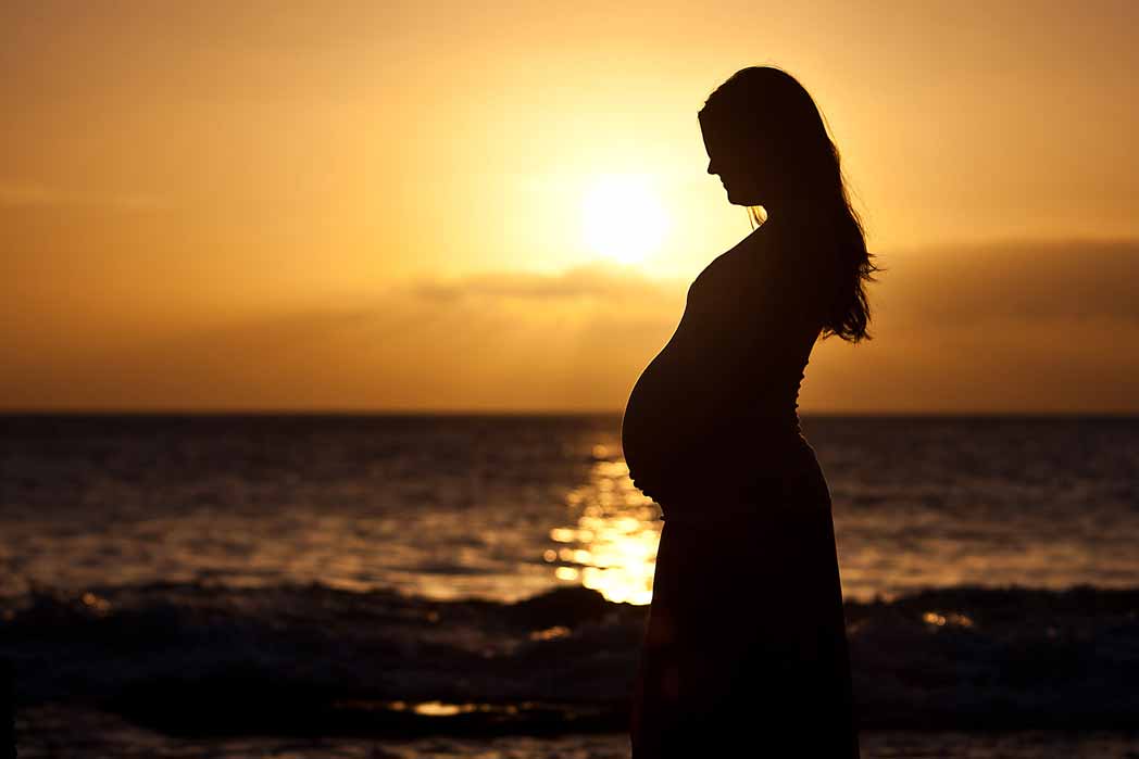 zwangere vrouw voor de zee bij zonsondergang