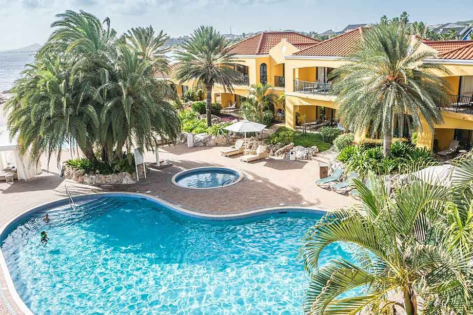 geel hotel met palmbomen bij zwembad