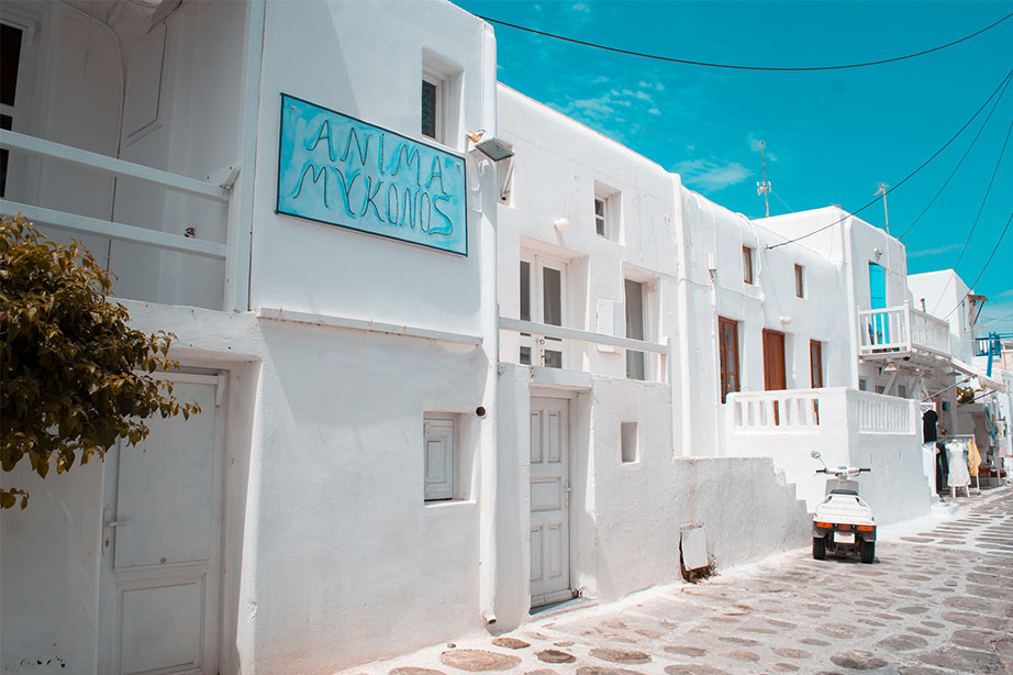 witte huisjes in een straat met azuurblauwe lucht en bord op Mykonos