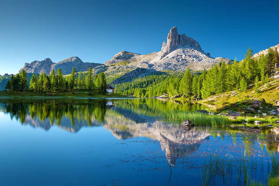 dolomiten meer met bomen en bergen en groene vlaktes bij blauwe lucht