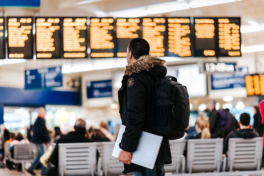 man op vliegveld met informatie op vertrekborden