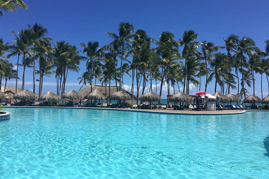zwembad met uitzicht op blauwe lucht palmbomen en rieten hutjes
