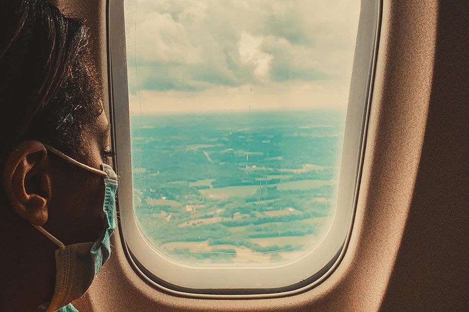 vrouw met mondkapje kijkt uit vliegtuig