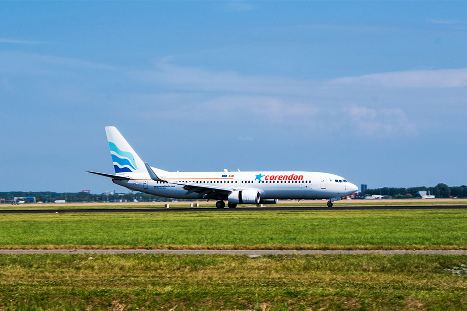 corendon vliegtuig landt op vliegveld bij blauwe lucht en groen grasveld