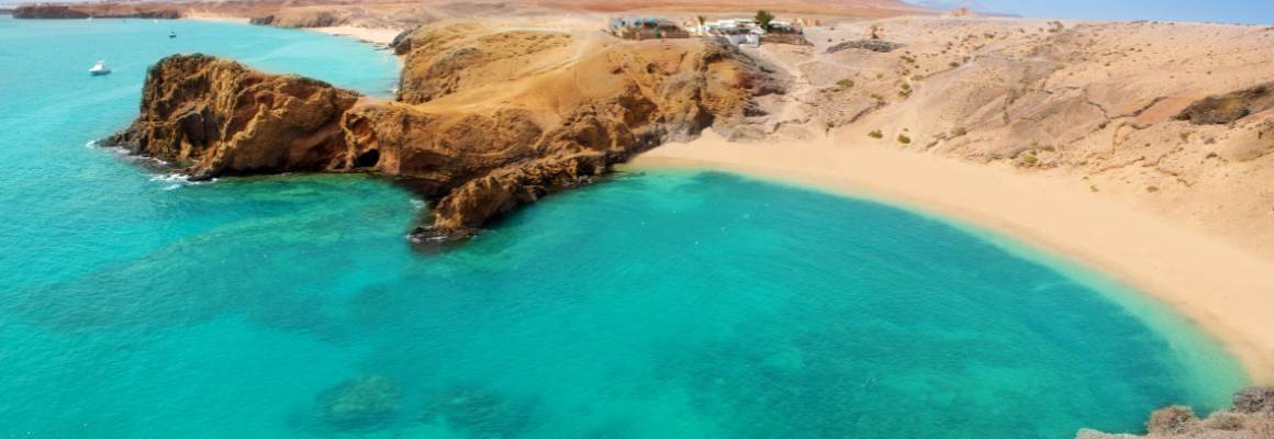 Uitzicht op het heldere turquoise water en het goudkleurige zandstrand van Playa de Papagayo op Lanzarote, omringd door rotsformaties.