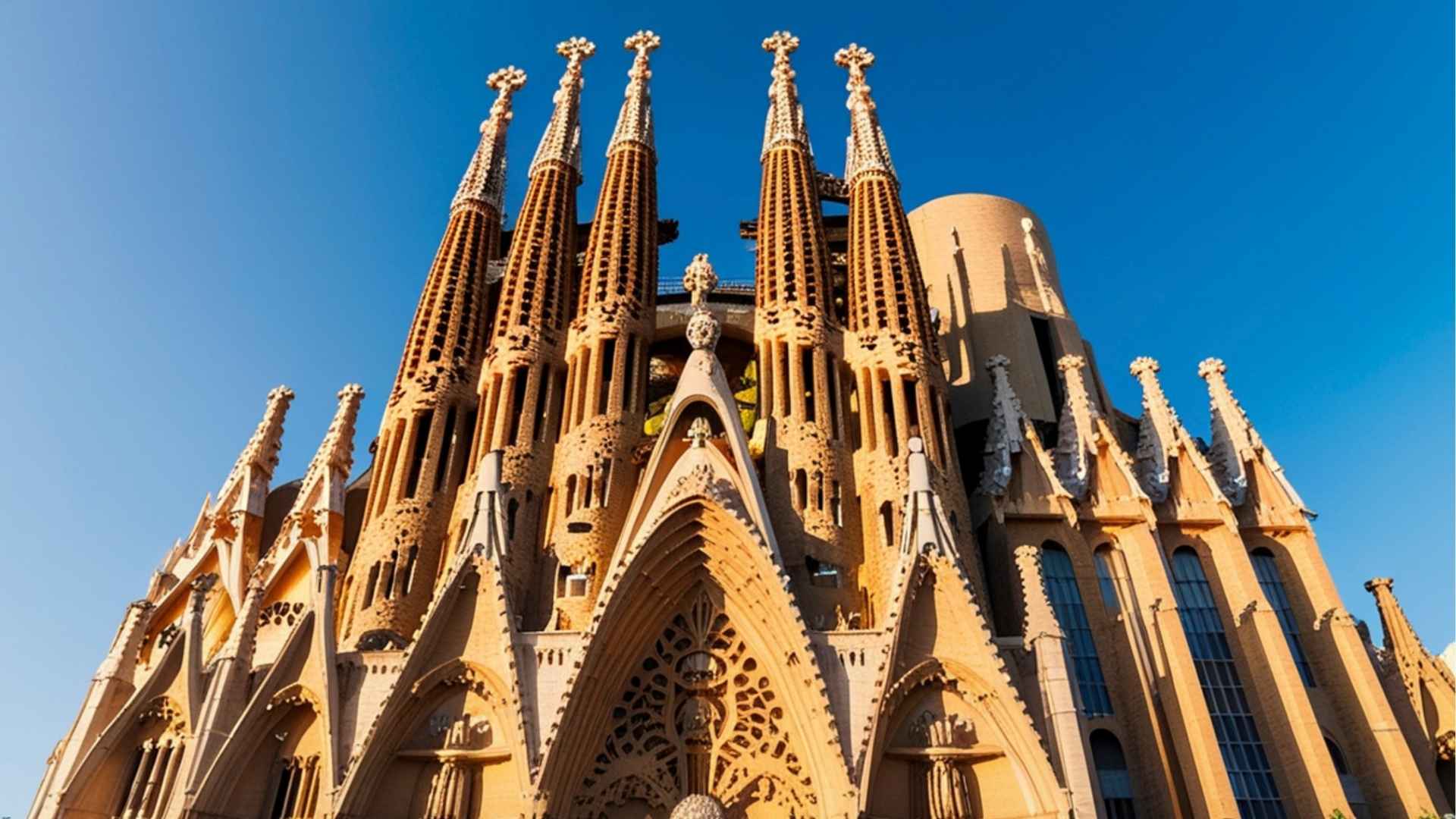 De Sagrada Família in Barcelona, Spanje, verlicht door de avondzon met een heldere blauwe lucht op de achtergrond. De iconische torens en gedetailleerde gevel zijn goed zichtbaar.
