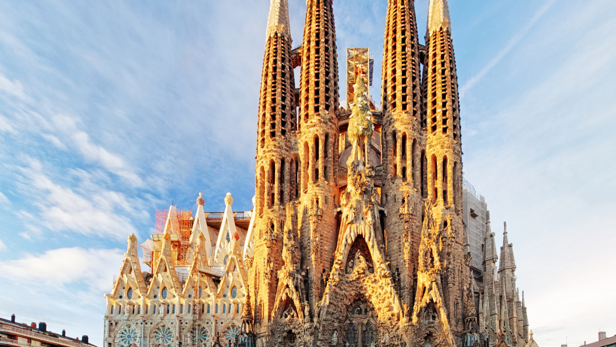 De Sagrada Família in Barcelona, Spanje, verlicht door de avondzon met een heldere blauwe lucht op de achtergrond. De iconische torens en gedetailleerde gevel zijn goed zichtbaar.