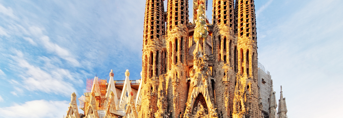 De Sagrada Família in Barcelona, Spanje, verlicht door de avondzon met een heldere blauwe lucht op de achtergrond. De iconische torens en gedetailleerde gevel zijn goed zichtbaar.