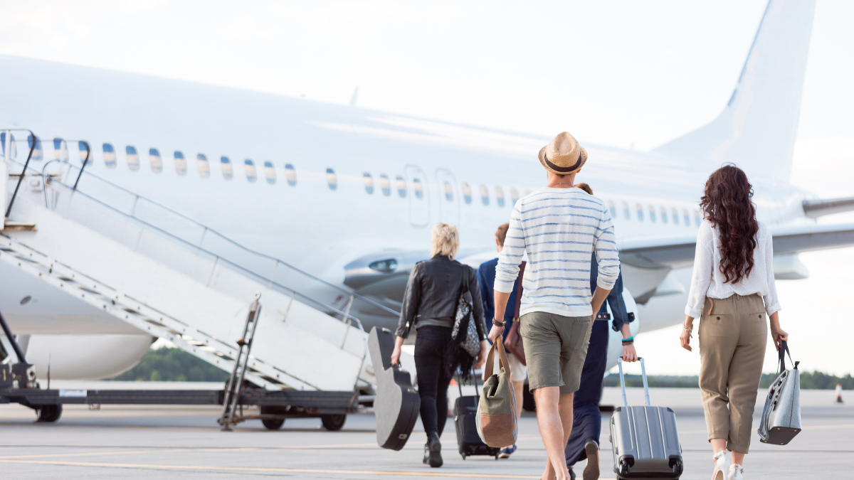 Passagiers lopen over het vliegveld richting een vliegtuigtrap om aan boord te gaan van een vliegtuig, met bagage in de hand