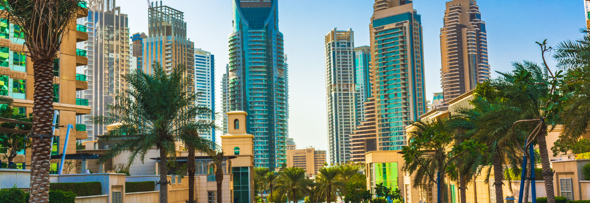 Moderne skyline met hoge wolkenkrabbers en palmbomen onder een heldere blauwe lucht, waarschijnlijk in een warme stad als Dubai