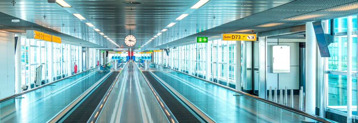 Lege loopband in een modern vliegveld met een grote klok in het midden en borden naar gate D73 en andere gates. De terminal is licht en ruim met veel glas en gele bewegwijzering